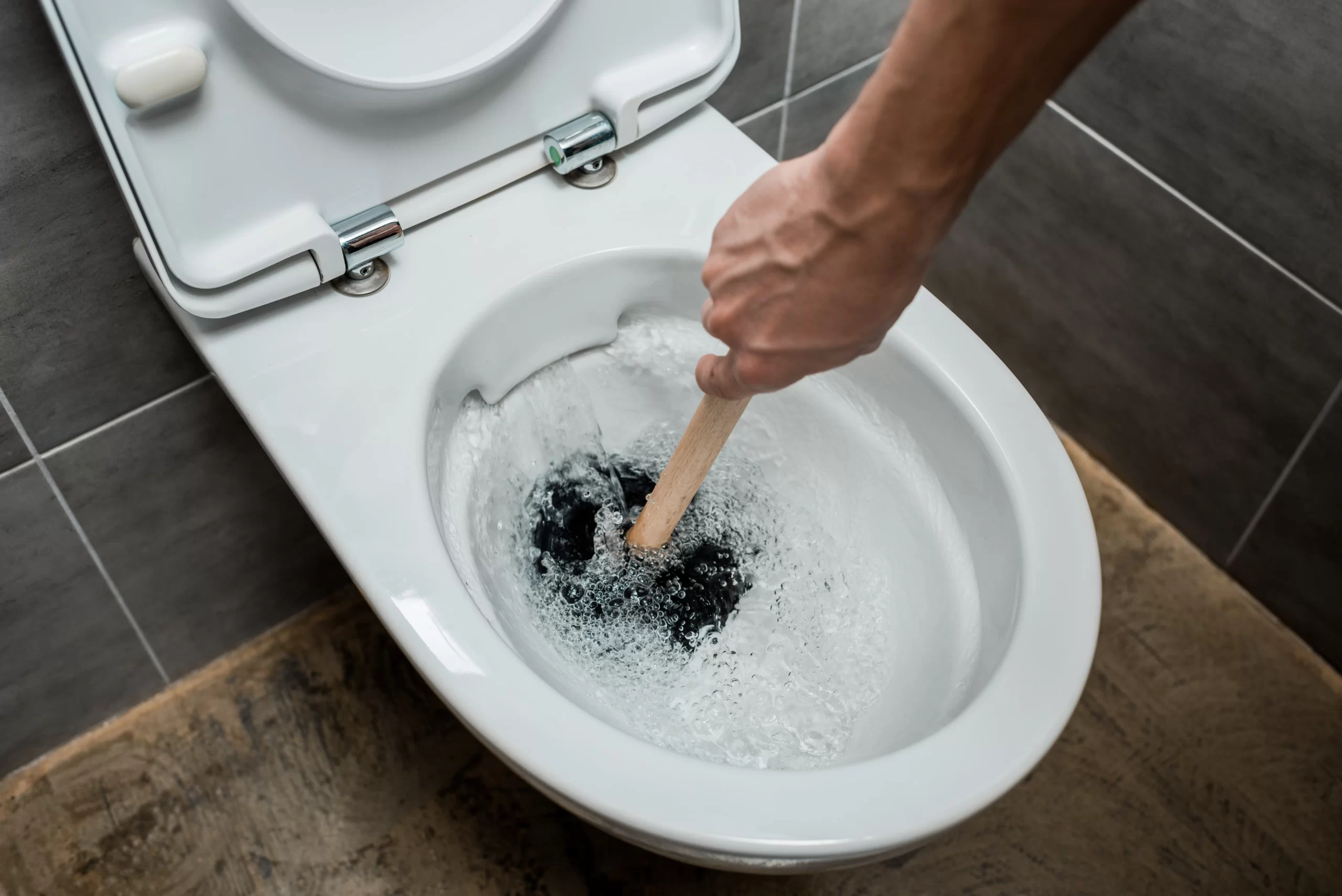 Commercial plumber unclogging a blocked toilet in a restaurant restroom.